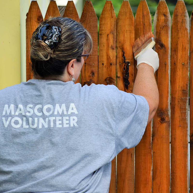 Woman with her back towards the camera while staining a fence. Words Mascoma Volunteer on back of shirt
